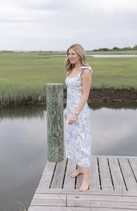 Woman stands on dock in floral dress.