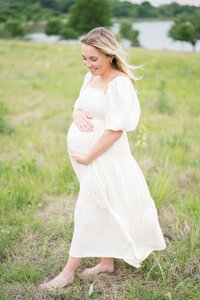 Pregnant woman in white dress stands in field