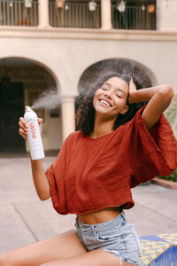 Model spraying Evian facial mist mid-motion in a Spanish-style courtyard