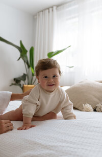 Bébé avec une sourire coquin assit sur un lit.