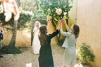 Bridesmaids tossing wedding bouquet outdoors while bride watches