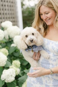 Woman in blue floral dress smiles as she hold a white dog.