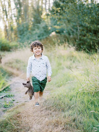 Little boy walking in the grassy field and holding his stuffy