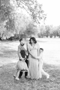 Black and white candid portrait of the Dilorio family laughing together as their children hug them during a playful outdoor photography session in Las Vegas.