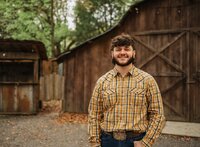 Senior portrait at Circle B Lake in Wilmer, Alabama — waist-up in front of an old wooden barn.