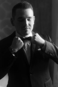 A groom in a classic tuxedo fixing his bow tie while preparing for his wedding ceremony in Prague.