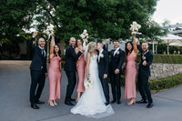 Wedding party dressed in pink and black cheering for the bride and groom who share a kiss in the centre. Outside Brindabella Hills Winery, Wallaroo NSW