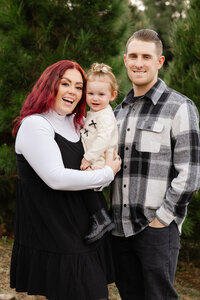 Mother and father smiling while holding their baby outdoors, candid natural light family portrait by Kaitlyn Dawn Photography, professional family photographer.