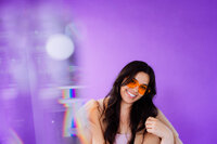 Playful singer-songwriter portrait with orange glasses against a purple studio backdrop