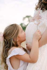 Toddler kissing her mom's pregnant belly in floral field, Miami maternity photos