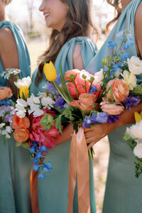 Close-up of colorful bridesmaid bouquets with tulips, roses, and delphiniums in bright spring colors, held by bridesmaids in light blue dresses at Burritt on the Mountain in Huntsville, Alabama, photographed by Perry Hancock.