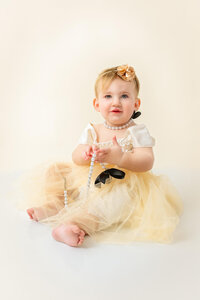 Baby in yellow dress seated on neutral studio background in Eastern North Carolina