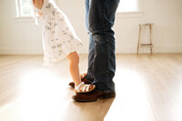 a little girl stands on her daddy's feet while dancing