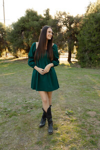 Young woman standing in a grassy park during golden hour wearing a green dress, outdoor lifestyle portrait captured by Kaitlyn Dawn Photography in Yucaipa.