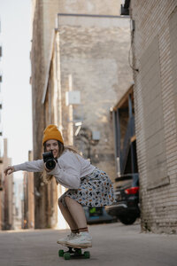 A person skateboarding in an alley while holding up a camera