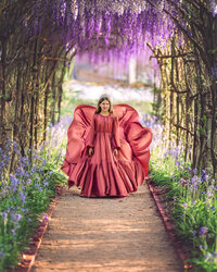 Young girl in flowing dusty pink dress beneath a blooming wisteria arch in a historic Tryon garden