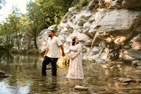 a couple walks hand in hand in the creek bed during their maternity session in frisco,texas.