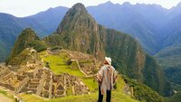 Man stands on green hill overlooking ancient ruins in the mountains