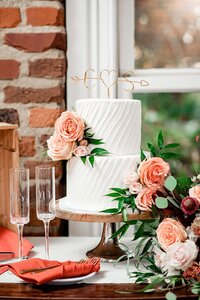 White two tier wedding cake with peach roses against an exposed brick background