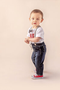 toddler standing in dark jeans and red sneakers during first birthday session