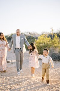 The Collins family walking together in the Las Vegas desert at golden hour, with parents holding hands with their children as they laugh and play during a candid outdoor family photography session.