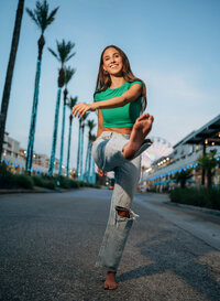Senior portrait at The Wharf in Orange Beach, Alabama — barefoot kick toward the camera,
wearing a bright green top and jeans.