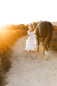 High school senior girl walking beside a horse at sunset in a natural field setting, Yucaipa lifestyle senior photography by Kaitlyn Dawn Photography.