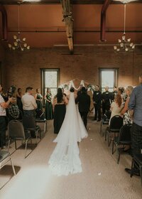 Bride walking down the aisle at a brick-walled indoor wedding venue