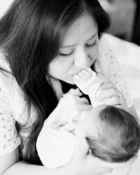 Black and white close-up of a mother kissing her newborn baby’s hand during an intimate in-home lifestyle session.