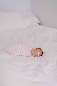 newborn baby girl wrapped in a pink swaddle and laying on a clean white bed
