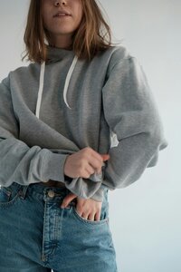 A person in a casual grey hoodie and blue jeans stands in a relaxed pose with a cropped view that focuses on the midsection.