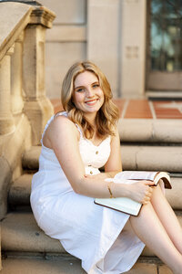 High school senior girl sitting on stone steps holding a book during golden hour, natural light senior portrait by Kaitlyn Dawn Photography.