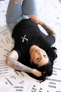 Tattooed woman with long dark hair lying on studio floor smiling playfully. Photograph by Yucaipa branding photographer Kaitlyn Dawn Photography.