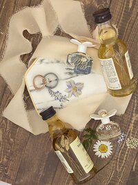 four mini bottles of perfume and whiskey bottles painted with florals and wheat stalks with wedding rings, dried flowers and silk ribbon scattered around them
