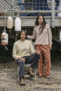 Cream and blush crewneck sweaters styled with corduroy trousers beneath a deck hung with buoys