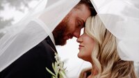 Bride and groom standing under the bride's veil looking at each other