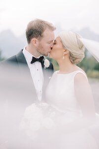 Blonde bride kissing her newlywed groom under a veil at Rendezvous Lodge