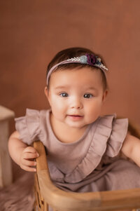 A baby girl sits in a woven basket for her portrait session in our Waukesha studio.