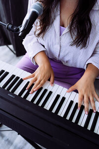 Close-up of a singer-songwriter playing piano with a microphone positioned above the keyboard