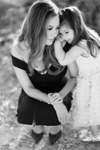 Black and white portrait of a mother and young daughter from the Parker family sharing a tender moment, with the child resting her head on her mother’s shoulder during an intimate outdoor session in Las Vegas.
