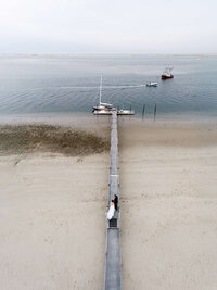 A striking drone view of a couple on a long wooden pier, preserving the atmosphere and emotion of a luxury coastal wedding.