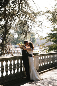 Newlywed couple embracing beside the stone terrace at Orleans House Gallery after their wedding ceremony, with soft sunlight filtering through the trees and a romantic garden backdrop.