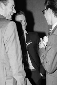 Candid documentary shot of well-dressed men in sharp suits at a luxury wedding reception, focusing on authentic interaction.