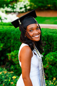 Senior wearing white dress and graduation cap smiling at camera during golden hour on Belmont University campus