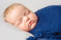 Close up of sleeping newborn boy in deep navy wrap during studio portrait session
