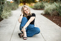 High school senior girl sitting casually on a walkway during golden hour with soft natural light, Yucaipa senior portrait by Kaitlyn Dawn Photography.