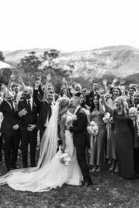 Bride and groom kiss in front of their family while they cheer