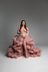 Studio maternity portrait of an expecting mother wearing a blush pink ruffle maternity gown photographed by Kaitlyn Dawn Photography.