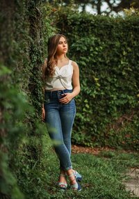 Senior portrait in downtown Mobile, Alabama — leaning against a wall of lush greenery looking to the side.