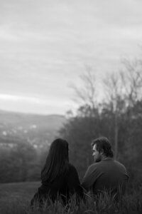 A couple sits together in the grass, cozy and calm during their engagement photoshoot in New England. Fine art lifestyle photography capturing romantic, and intimate photos.